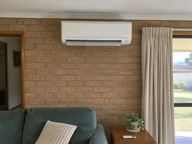 White split-system head on a brick wall above a lounge chair, louvre open in Para Hills